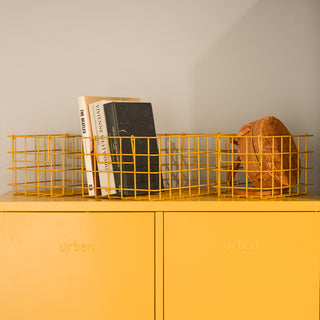A set of three mustard metal baskets containing books and a bag, on top of a yellow storage locker.