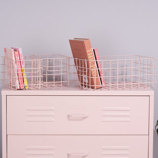 A set of three light pink metal baskets containing books, on top of a light pink set of metal drawers.